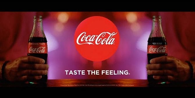 2 Coca-Cola Flaschen werden von 2 Menschen gehalten , das Coca-Cola Logo, der Slogan: Taste the Feeling.