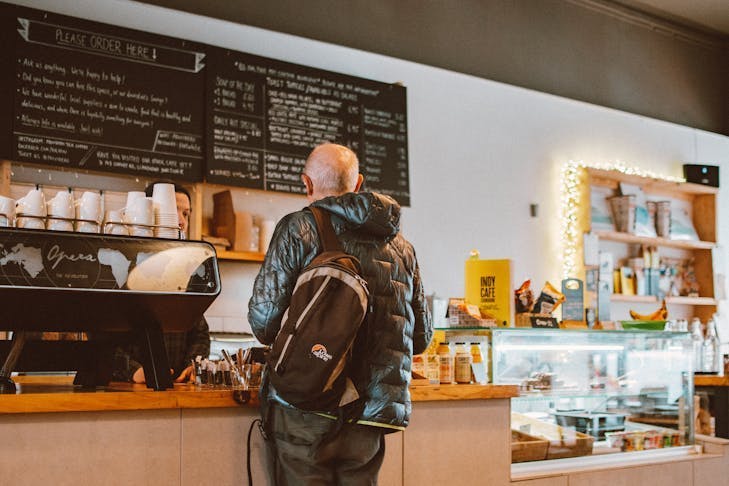Ein Mann steht vor einer Kaffeebar und schaut auf die Getränketafel.