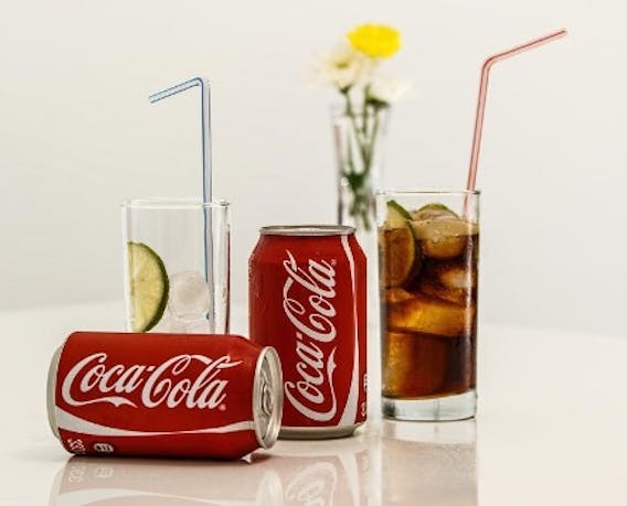 Coca-Cola blikjes en glazen staan ongeorganiseerd door elkaar heen op een tafel.