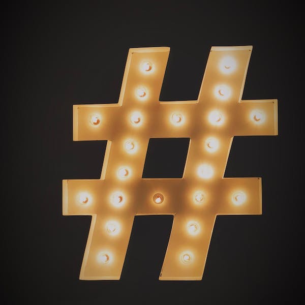 Hashtag symboli mustalla taustalla ja koristeltuna kirkkailla lampuilla.