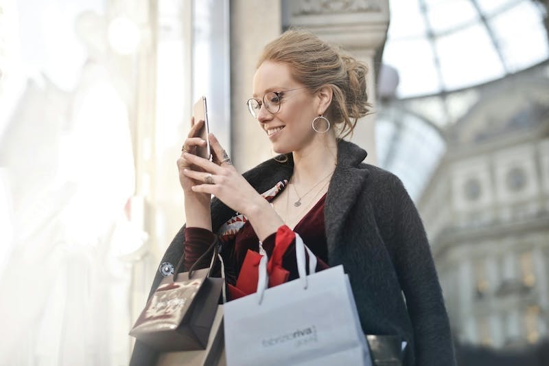 Eine junge Frau hält Shopping-Tüten und ihr Smartphone in der Hand