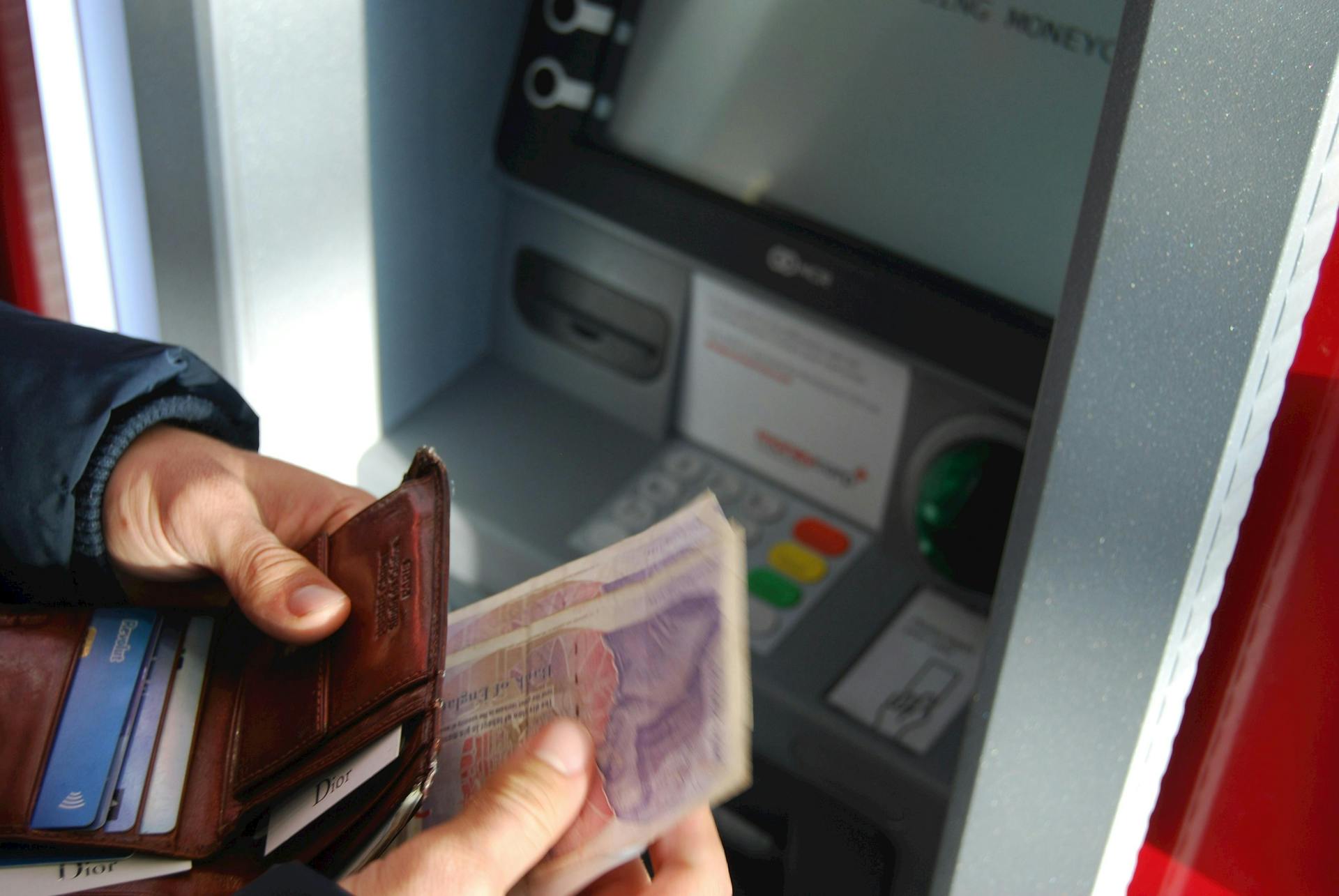 person at a bank atm with bank notes in a wallet