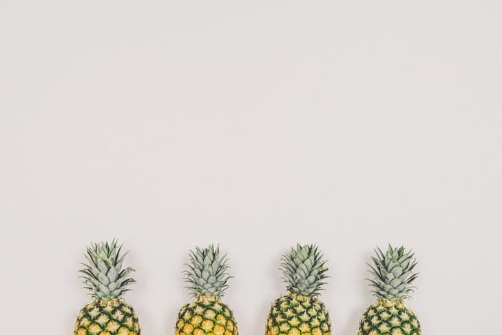 Vier Ananas stehen aufgereiht vor einer weißen Wand.