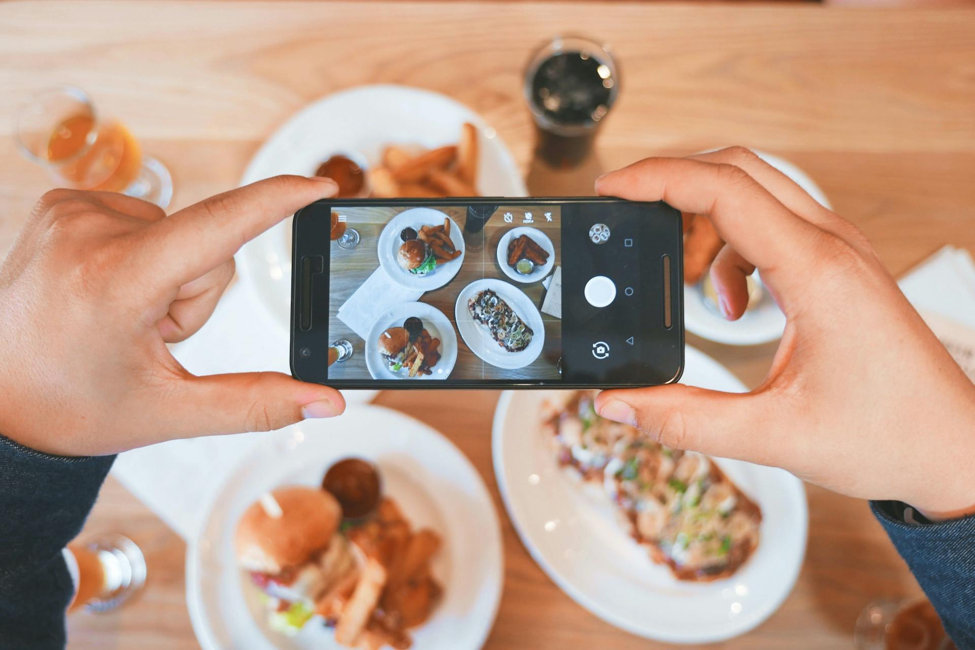 person holding a phone from above and taking a photo of food on the table