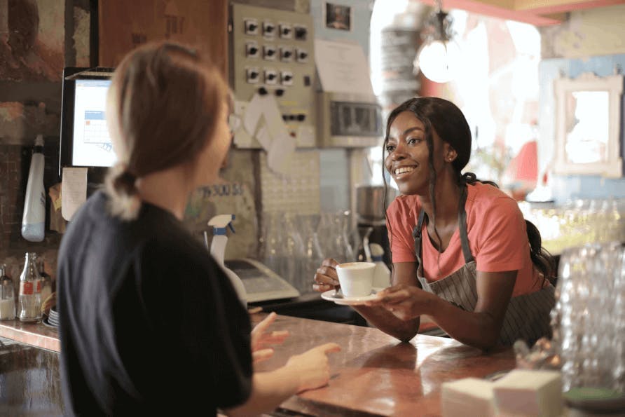 Een vrouw serveert een kop koffie aan een klant en lacht daar vriendelijk bij. Deze vrouw zet de persoonlijkheid van haar merk kracht bij door daar ook naar te handelen. In dit geval door vriendelijk te lachen bij het serveren van de koffie