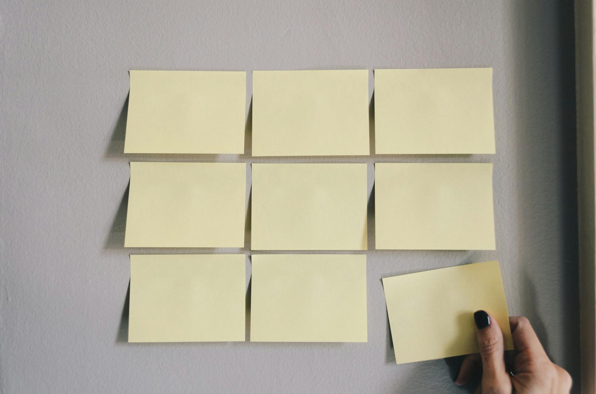 Grid of blank sticky notes with woman's hand adding final sticky note to the bottom row.