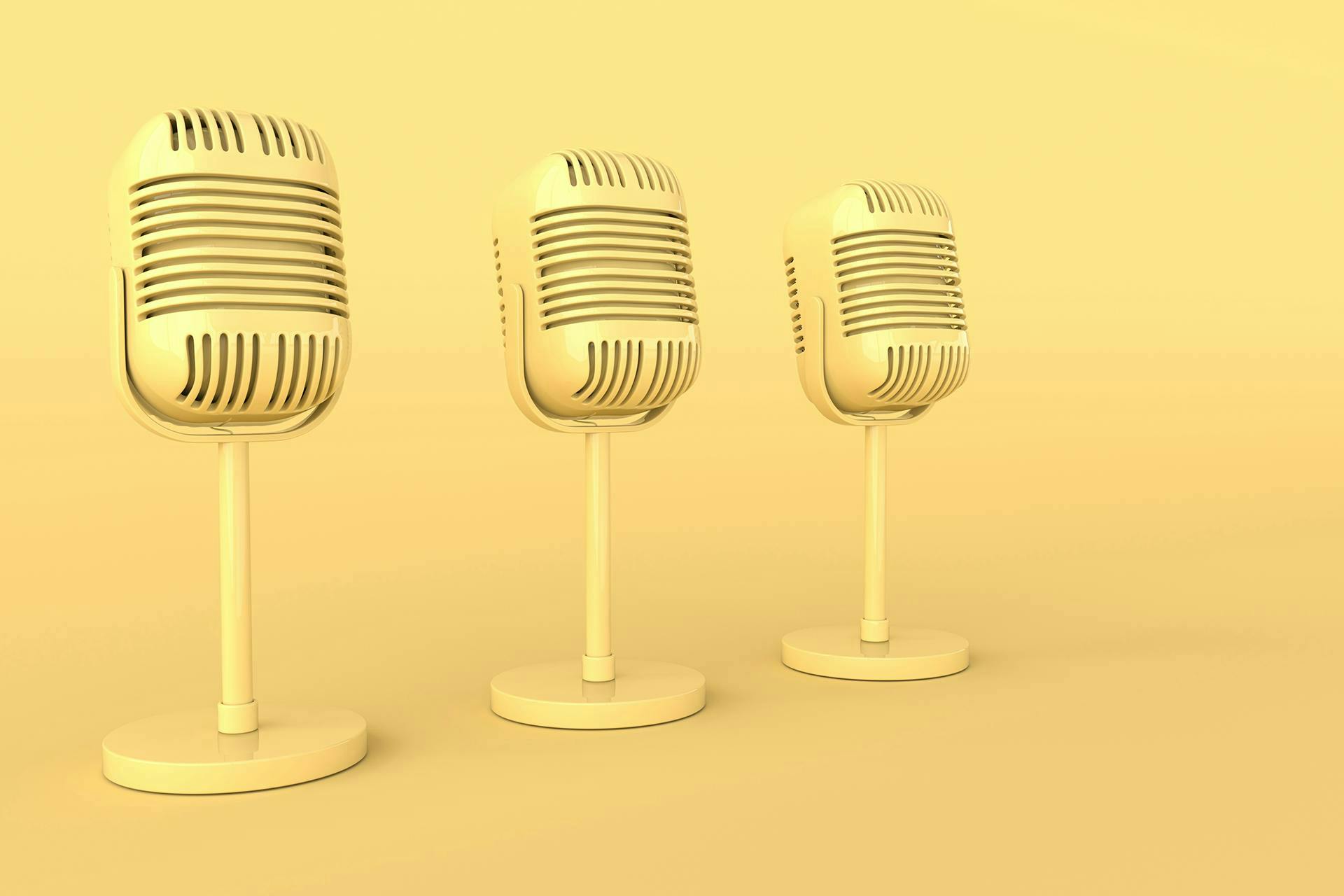 Drie gele microfonen staan naast elkaar tegen een gele achtergrond als een metafoor voor dat persberichten en PR en goede microfoon kunnen zijn om je doelgroep te berijken