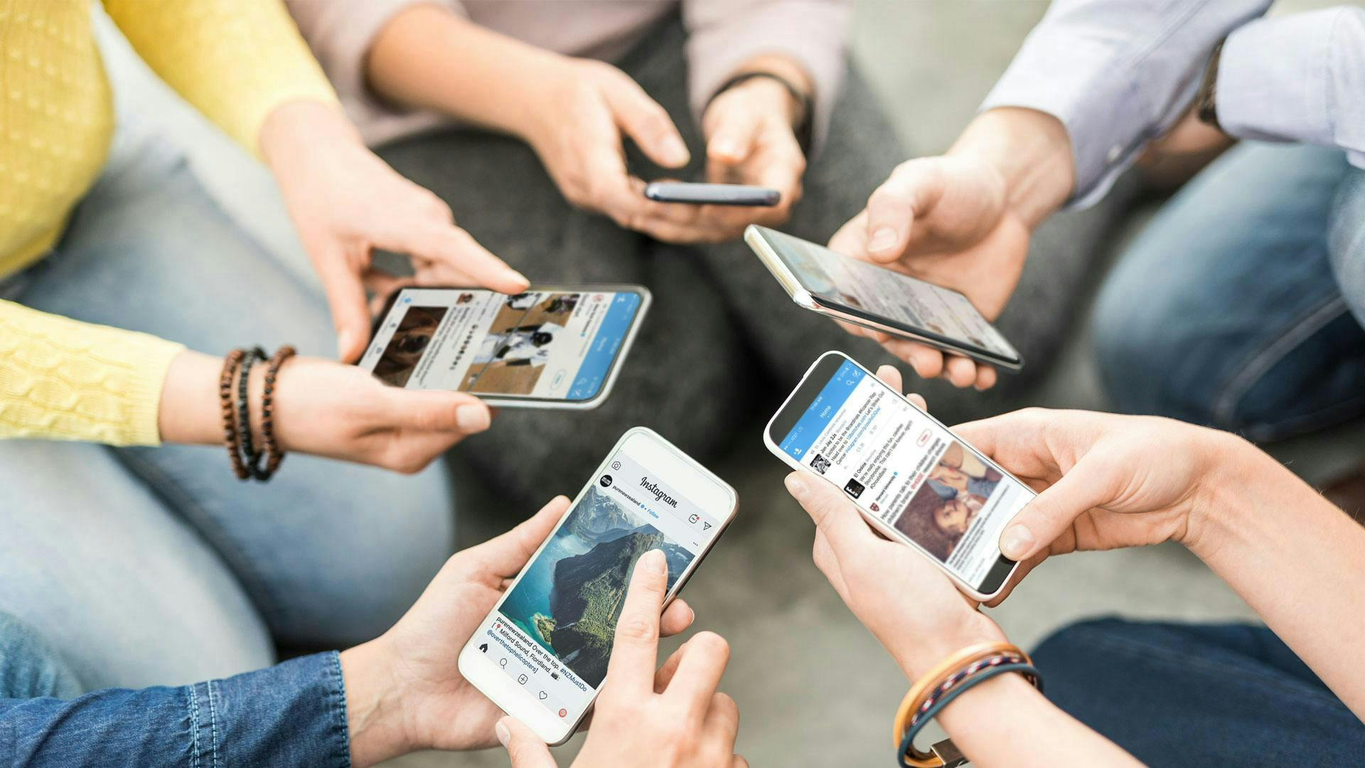 Photo of people sitting in a circle holding their smartphones into the middle