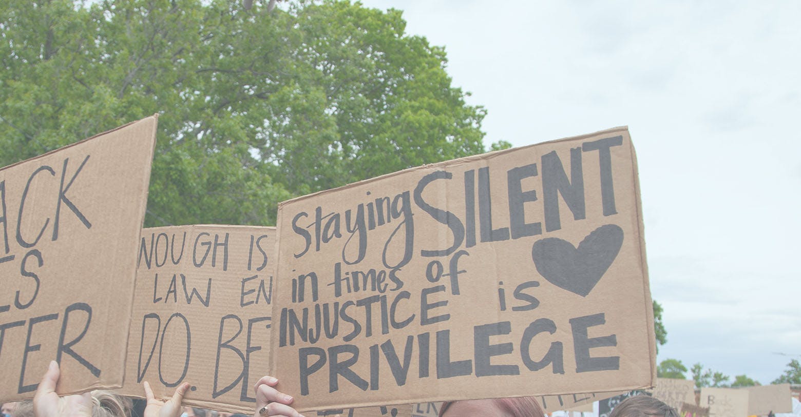 People holding signs at a protest. One sign reads "Staying silent in times of injustice is a privilege". 