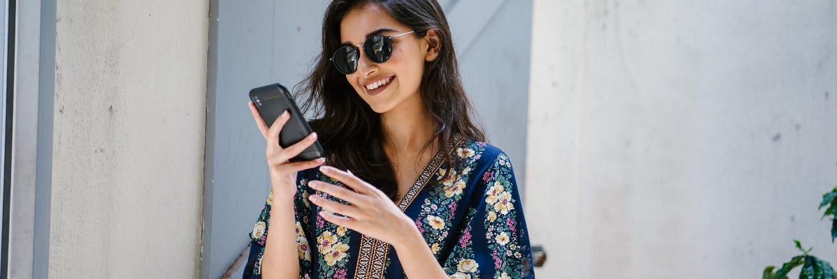 woman wearing sunglasses and smiling at her phone