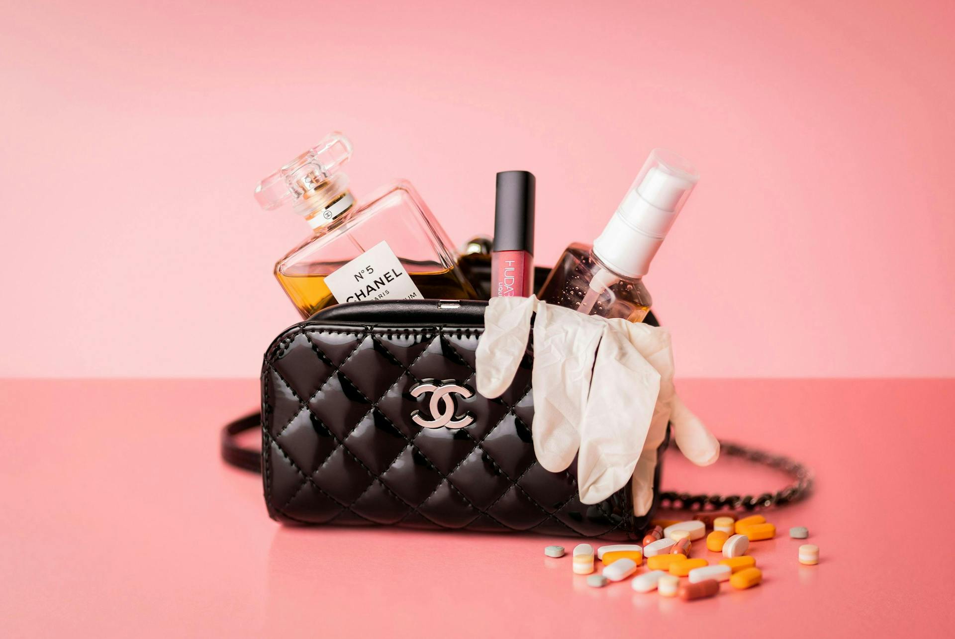Een afbeelding van een chanel tas met verschillende chanel producten erin tegen een roze achtergrond. Chanel heeft een erg sterk corporate brand waardoor je, wanneer je aan chanel denkt, je meteen aan al deze producten denkt.