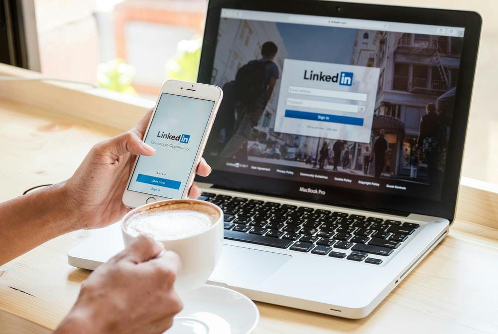 Mit Kaffe vor Laptop und Smartphone mit LinkedIn
