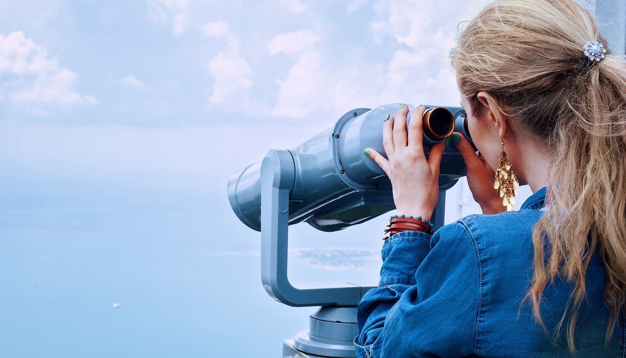 Woman looking through binoculars toward land far away.