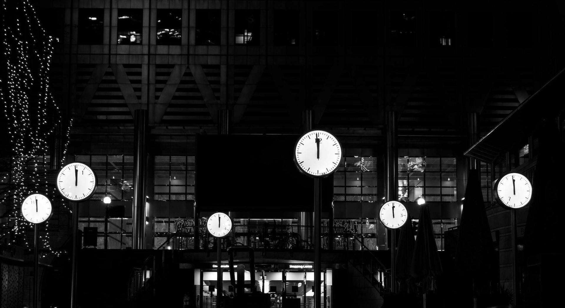 Black and white photograph showing multiple clocks glowing at night.