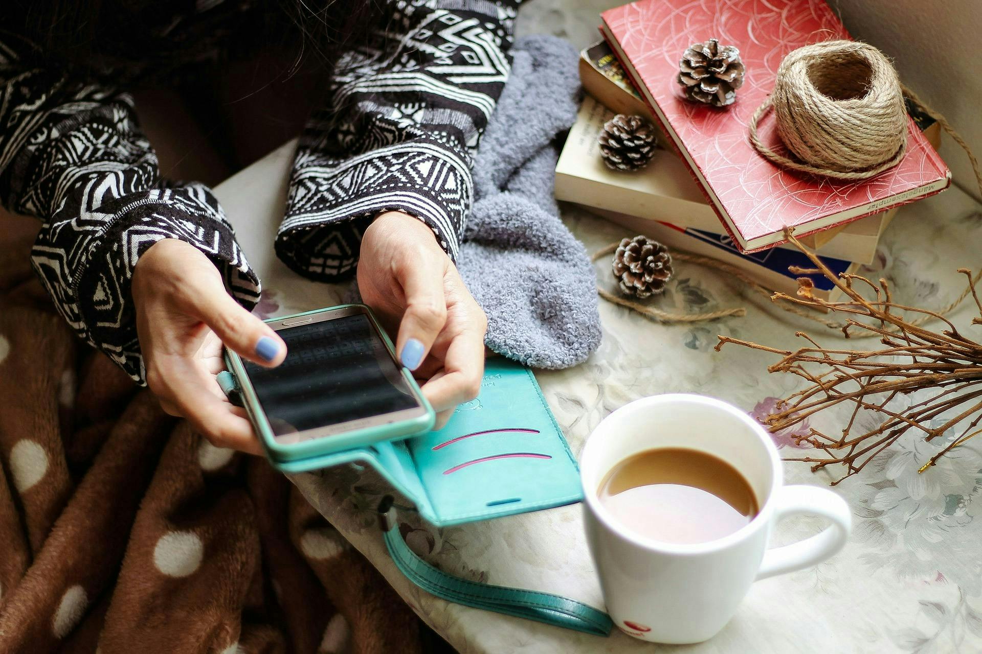 Person looking at a phone with a cup of coffee and books. You can tune-in to live shopping streams from multiple different social media platforms.