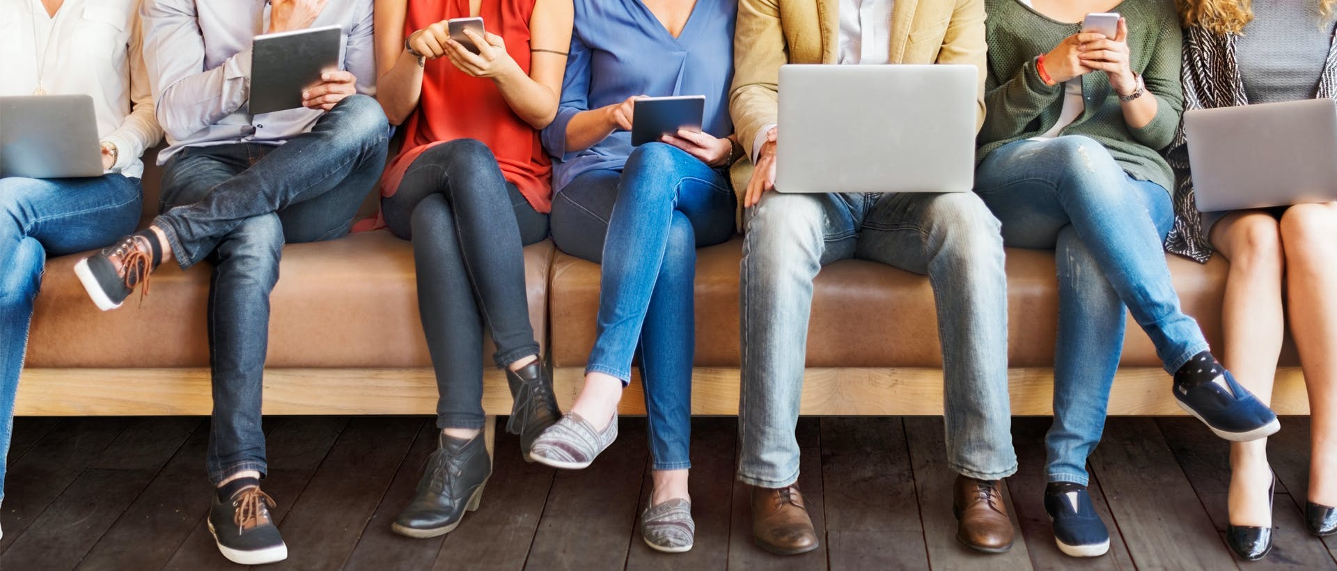 Een groep mensen zit op een bank terwijl ze op hun laptop. tablet of telefoon kijken