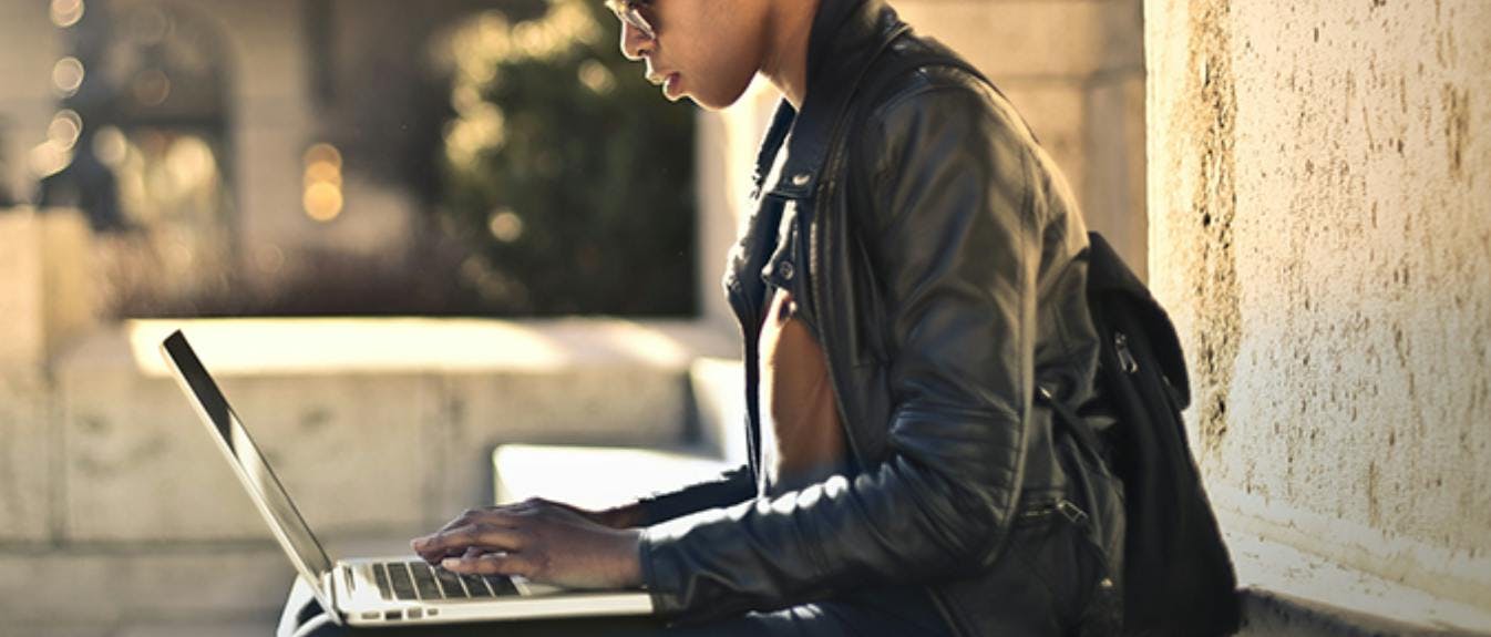 Foto einer Person, die draußen an ihrem Laptop arbeitet
