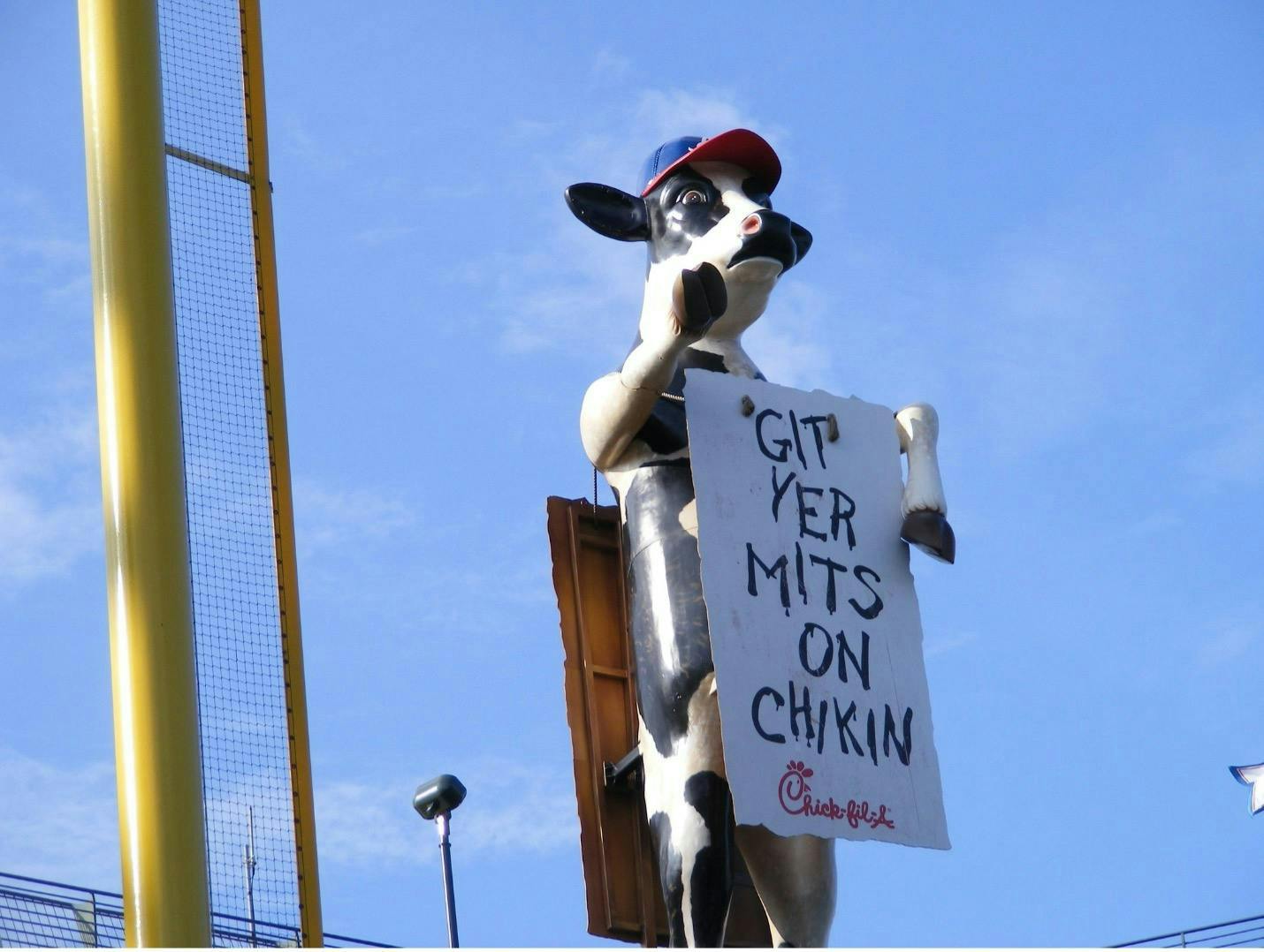 An outdoor billboard for Chick-Fil-A of a giant cow holding a sign that reads, "Git yer mits on chickin".