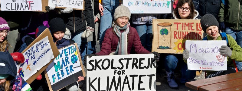 Greta Thunberg stands amongst a group of individuals holding signs about climate change