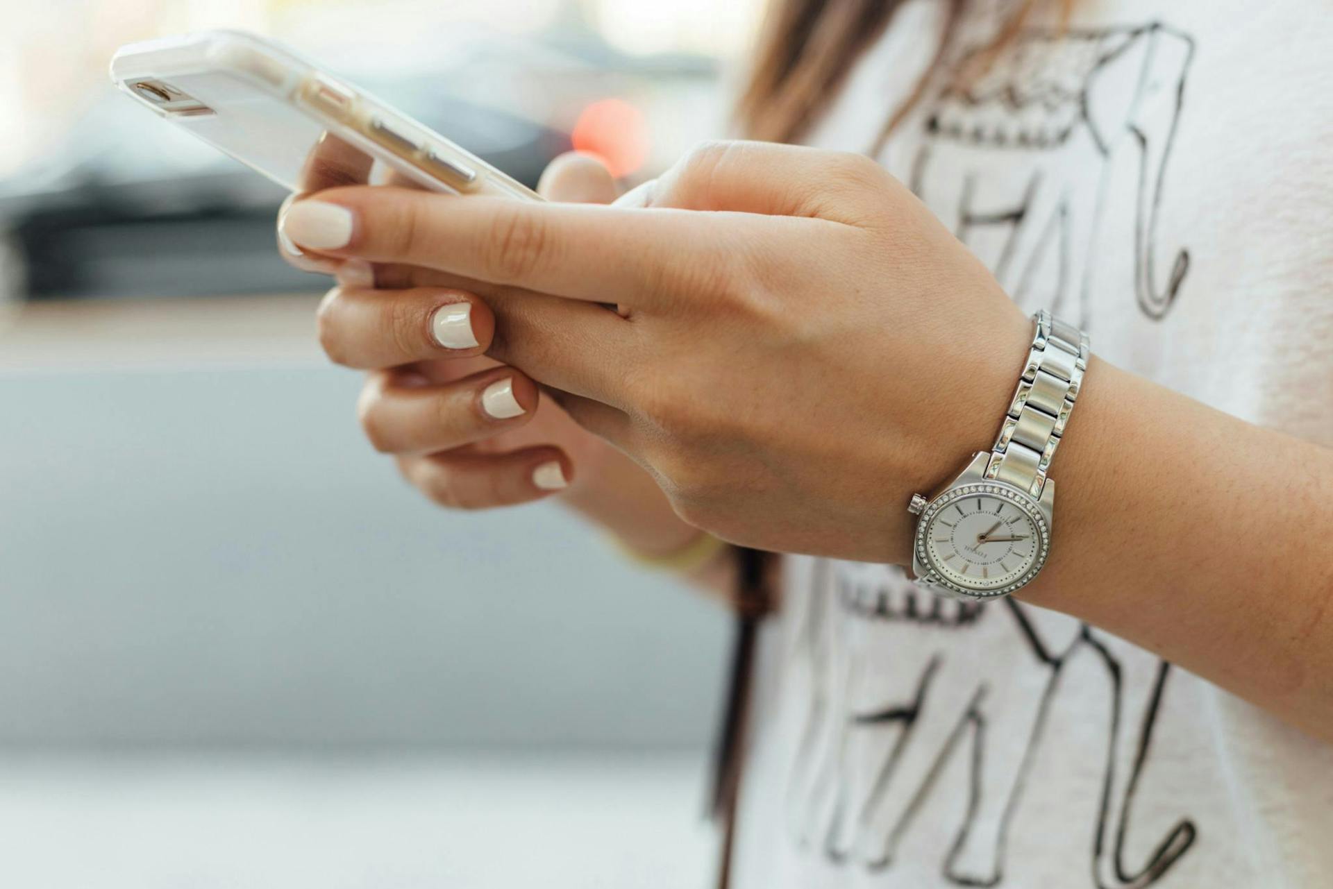woman with a silver watch typing on her mobile phone