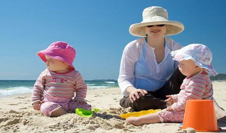 Twee babies met hun moeder spelen op het strand 