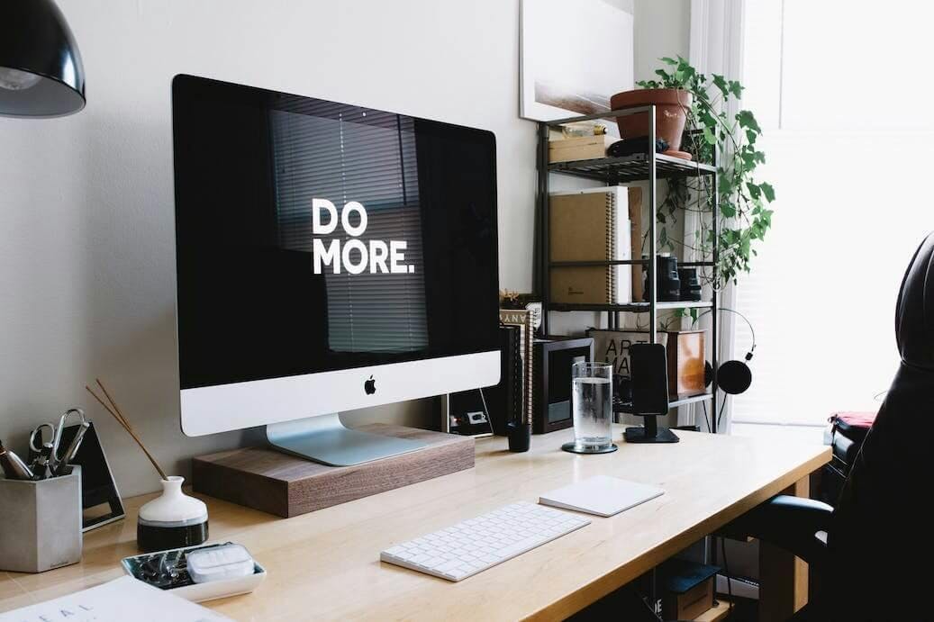 Man sieht einen Arbeitsplatz. Auf dem Schreibtisch steht ein iMac, auf dem "Do More" geschrieben steht. Das Bild leitet unseren Paragraphen mit fünf Tipps für eine Benchmark-Analyse ein.