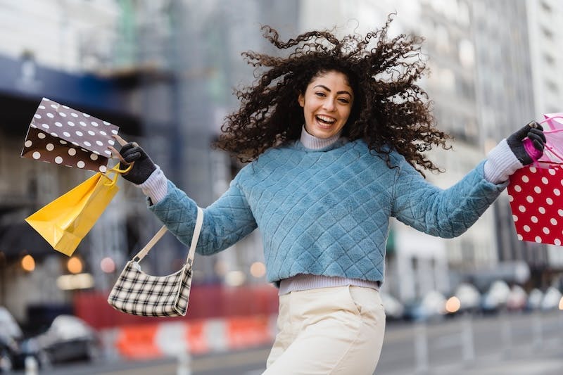 Eine junge Frau lacht und hält verschiedene Einkaufstüten in der Hand