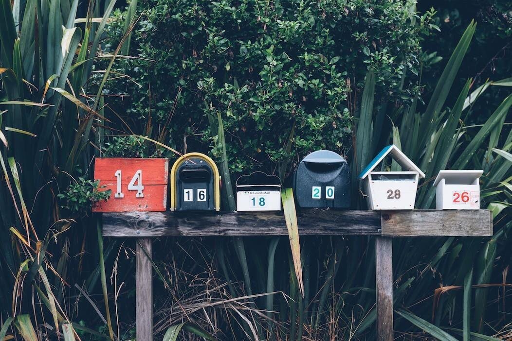 Man sieht ein Foto von mehreren hübschen Briefkästen, die auf einer Bank nebeneinander stehen.
