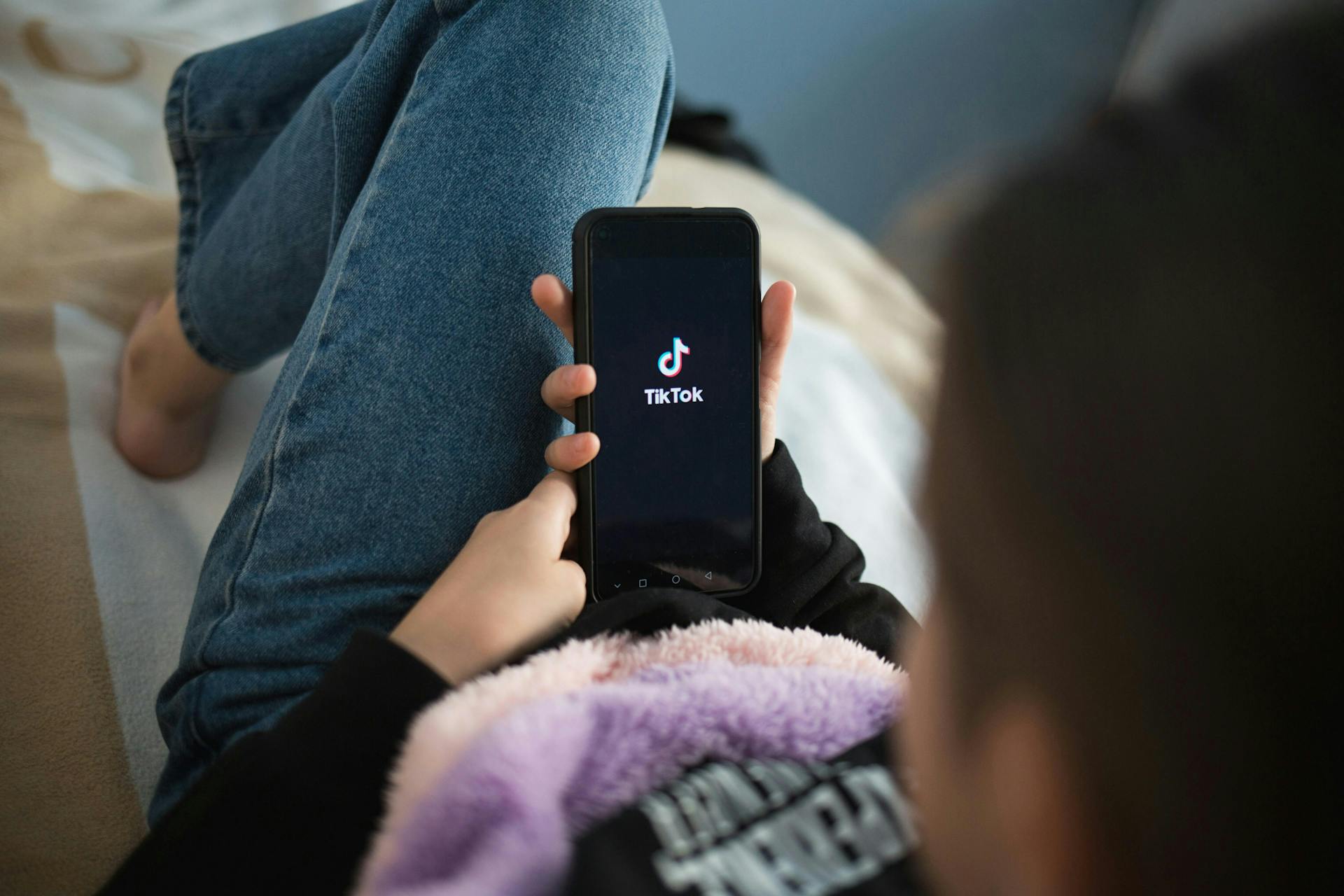 Image of a woman relaxing on a sofa, holding a smartphone displaying the TIokTok logo.
