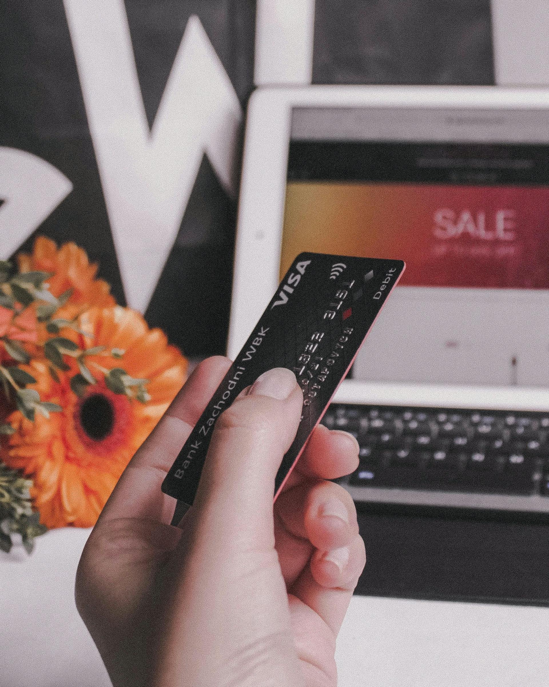 une personne tient une carte de crédit dans la main, devant elle se trouve un ordinateur affichant une page internet de vente