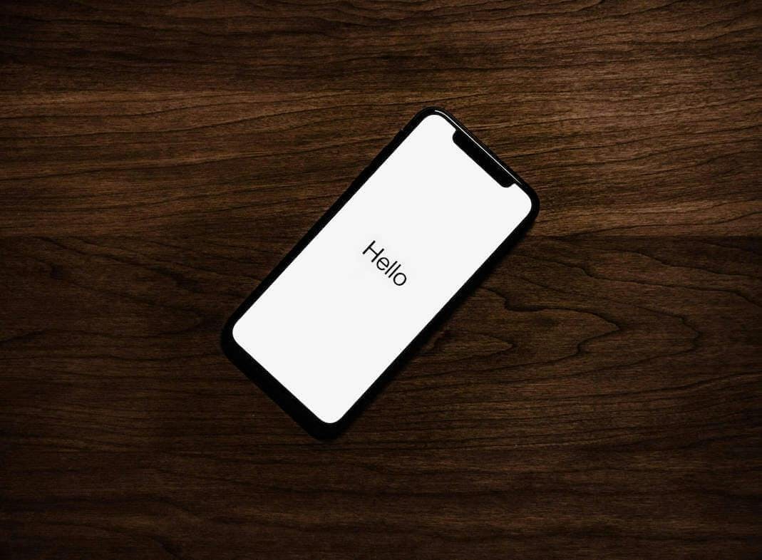 Man sieht ein Apple iPhone auf einem Holztisch liegen, das gerade eingerichtet wird. Denn man sieht das Wort “Hallo” auf dem Display.