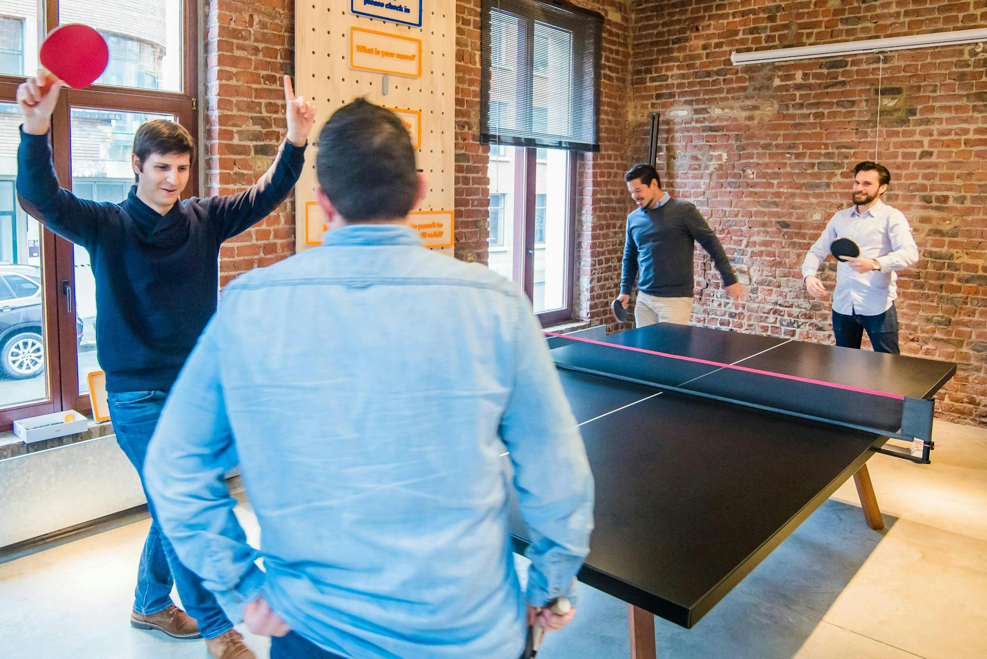 Vier mannen spelen ping-pong op kantoor. Dit is een voorbeeld van een activiteit die een goede bedrijfsreputatie opleverd en goede employee brand op kan leveren.