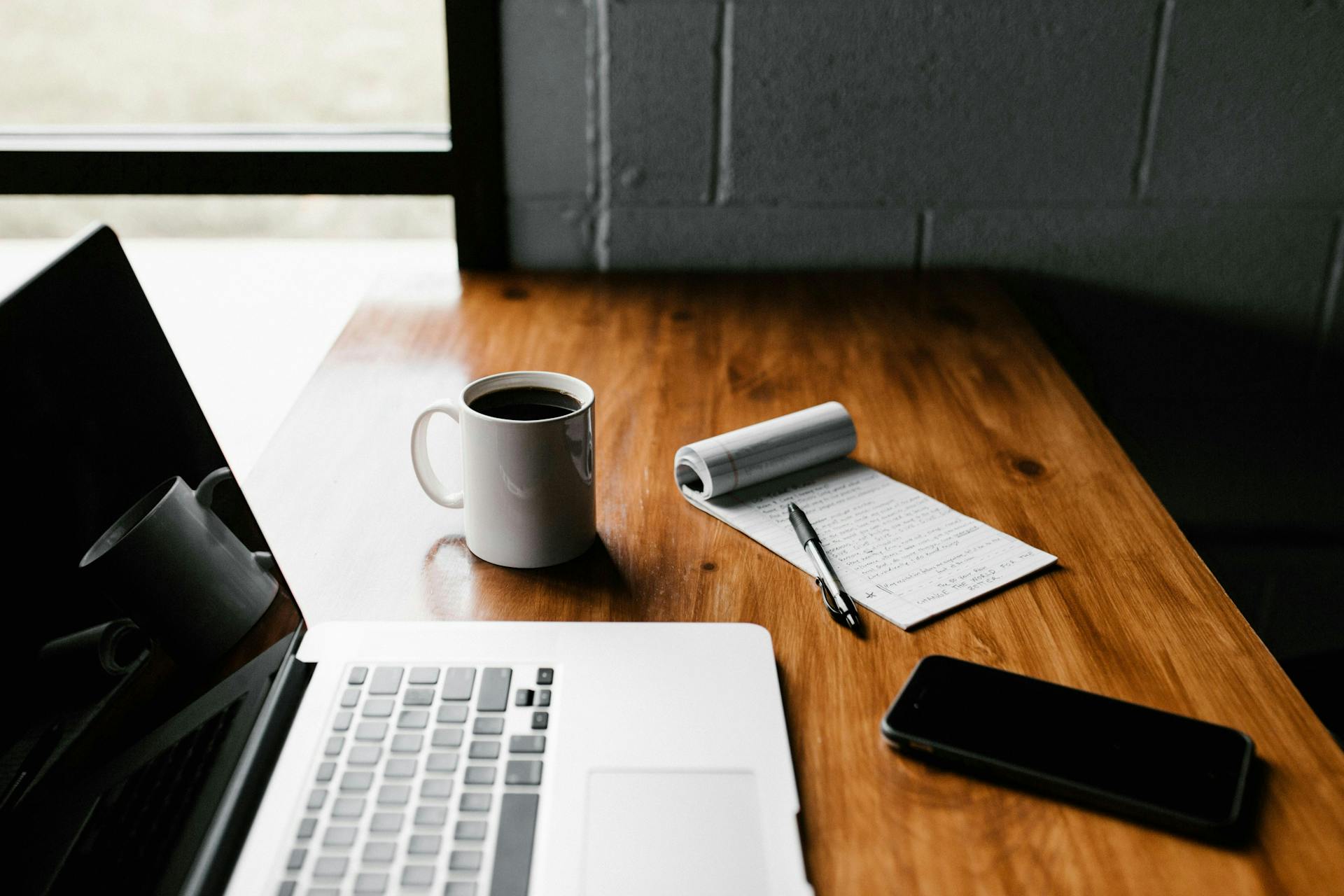 Der Schreibtisch eines Bloggers mit Laptop, Kaffeetasse, Notizbuch und Handy.  Mit Bloggern zusammenzuarbeiten kann für eure Social Media Strategie sehr gut sein.