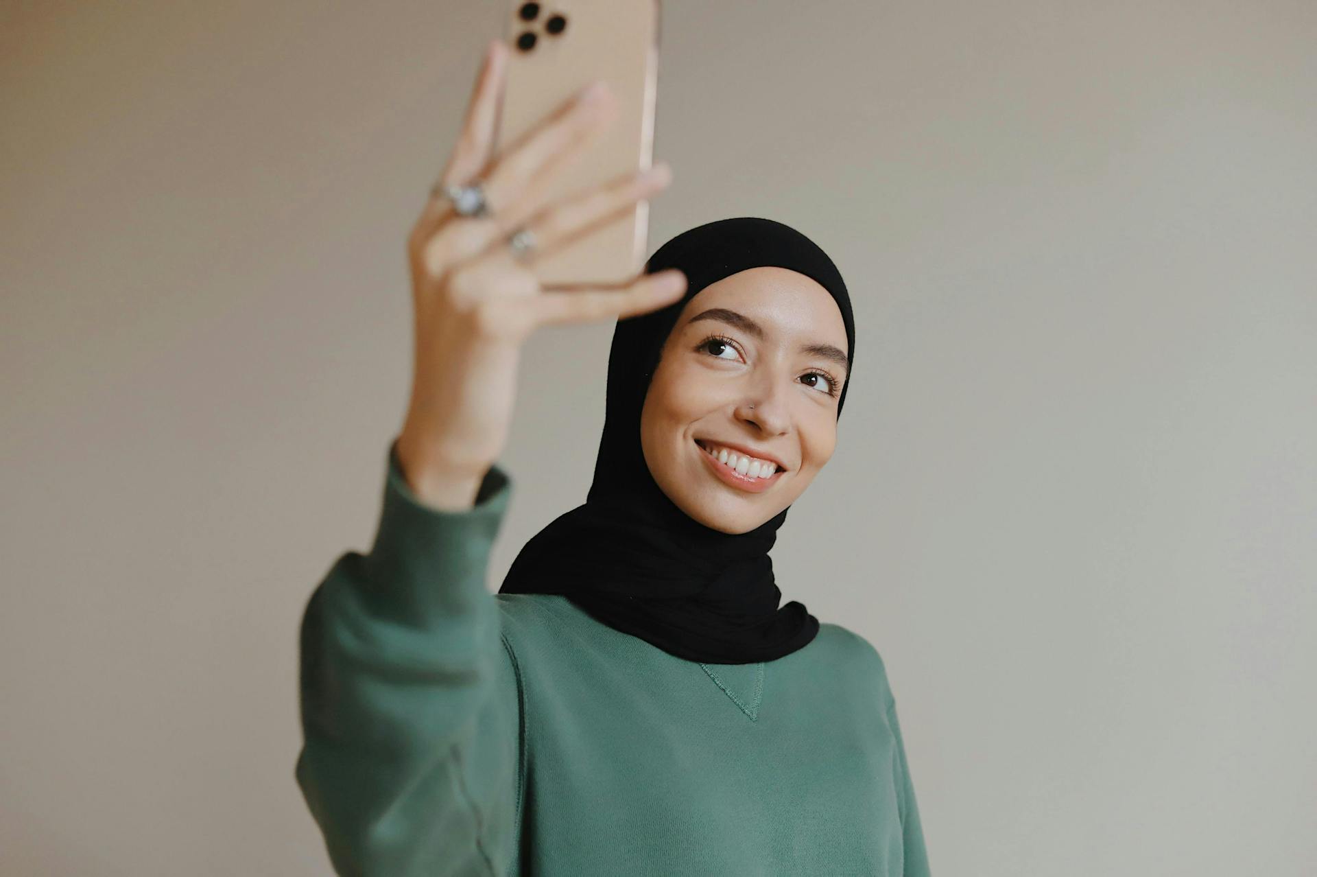 smiling middle eastern woman holding up an iphone to take a selfie