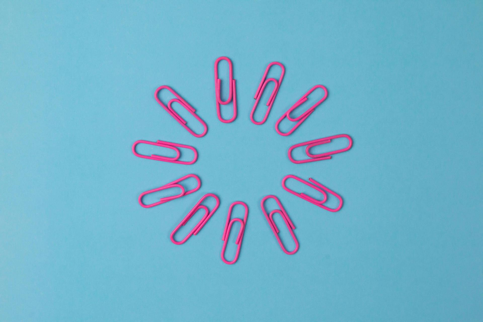 Circle of pink paper clips on a blue background. Don't get lazy with linking when writing a blog post 