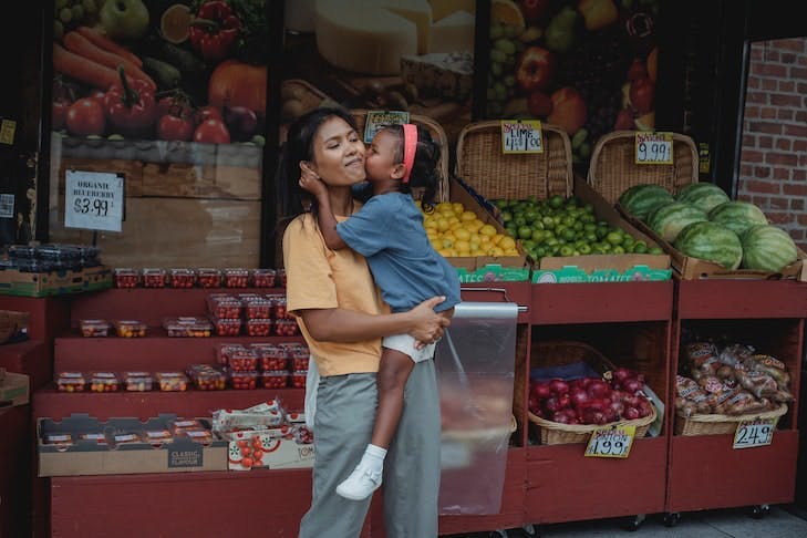 Une mère tient son enfant dans les bras et se tient devant une épicerie.