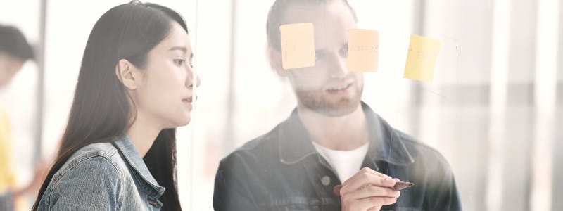 two people with sticky notes on glass wall for planning a facebook marketing strategy