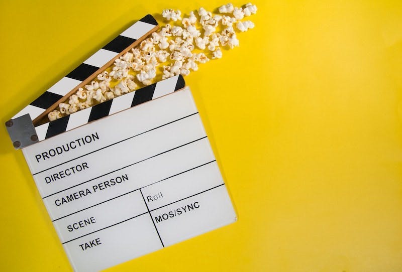 A clapperboard on a yellow background, popcorn is coming out of it