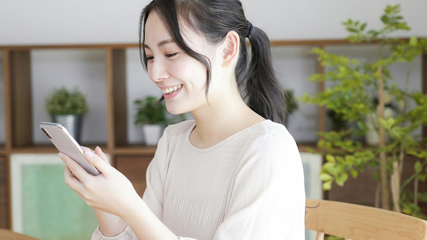 Image of a smiling woman holding a smartphone in her hand.