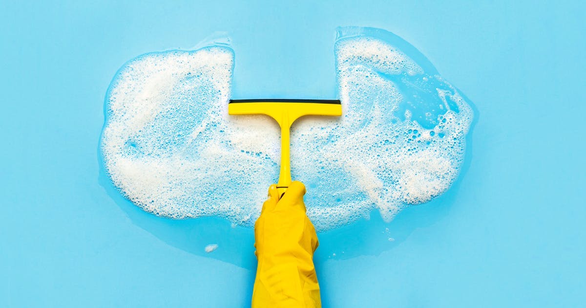 A person wearing a yellow glove holding a squeegee and wiping away a section of bubbles that are in the shape of a cloud. Today, most marketers store their customer data on a cloud-based software, which is why this image was selected for this blog by Meltwater on how to clean your cloud-based data. 