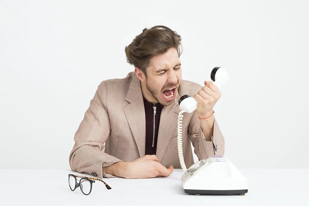 A frustrated consumer angrily shouting into an old style telephone, unhappy with the customer service he is getting. 