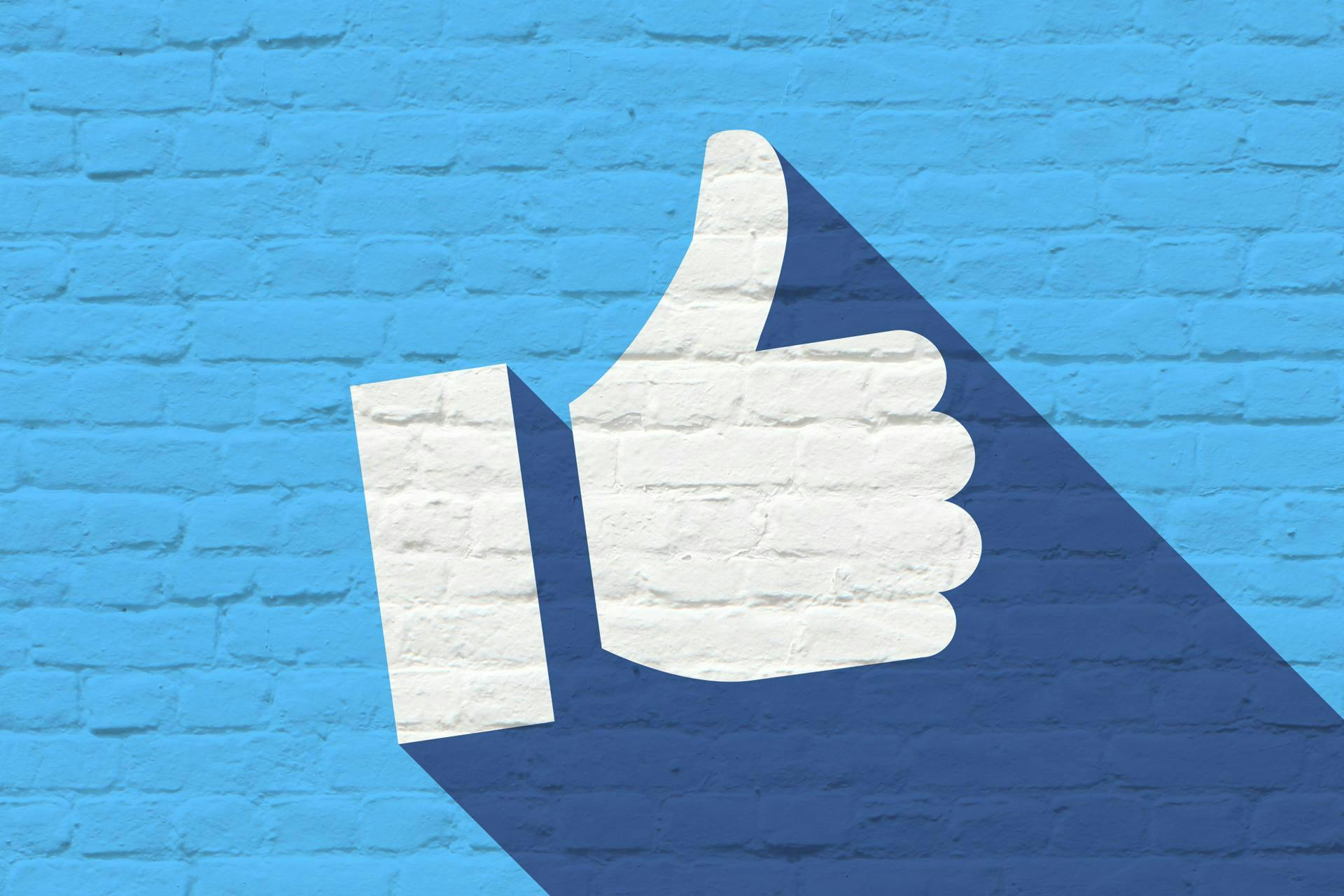 Un "like" blanc facebook sur un mur de brique bleu