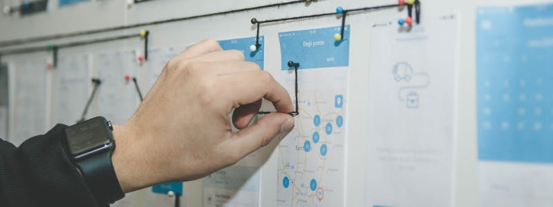 person pinning a black thread on white and blue paper on a board