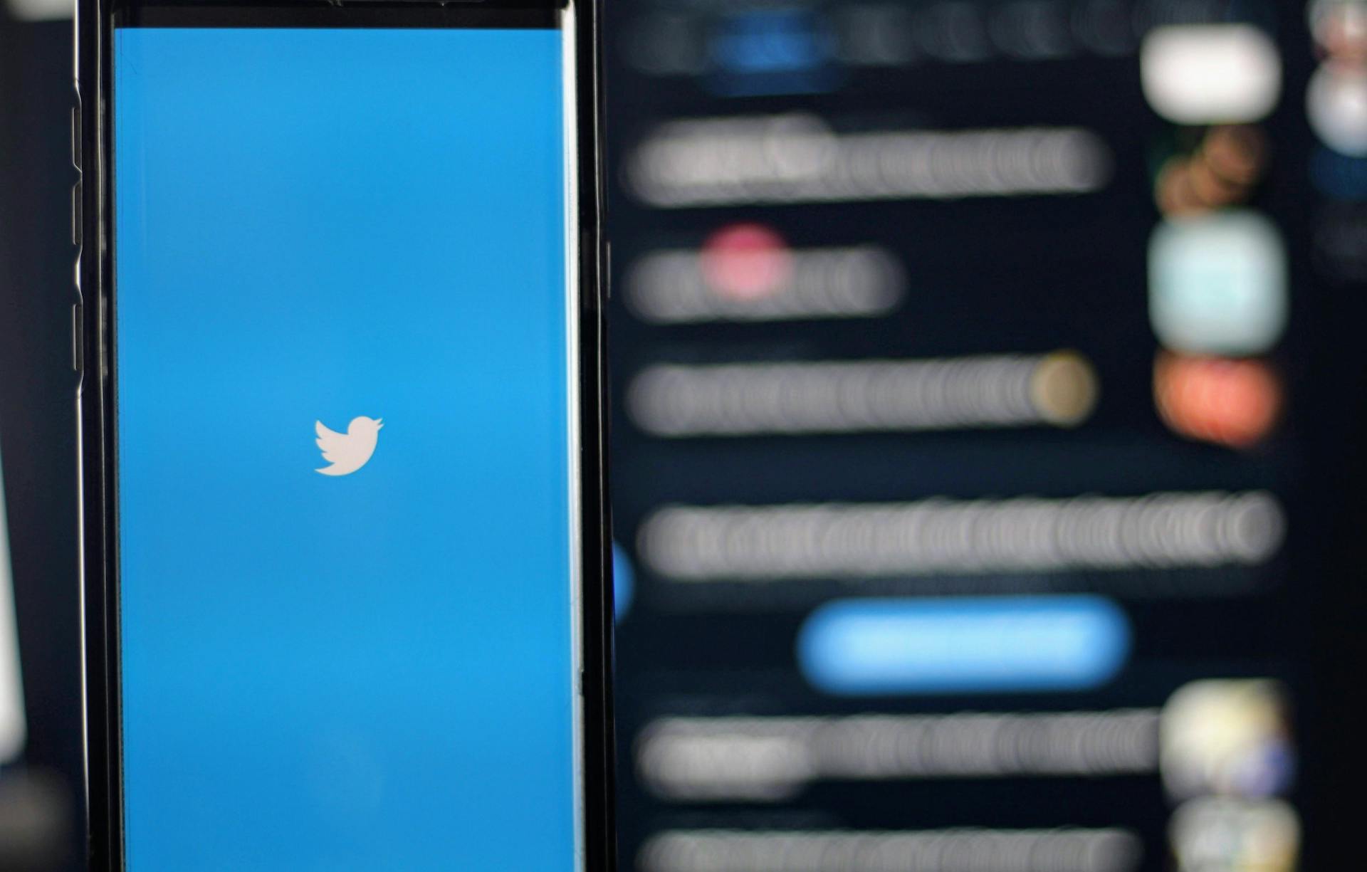 Phone screen showing Twitter logo next to out of focus Twitter home screen