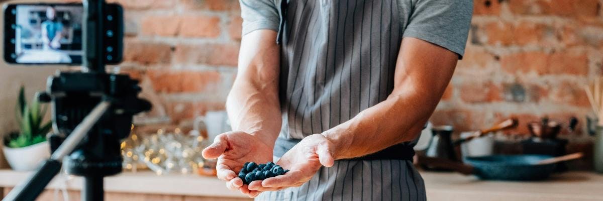 Micro influencer standing in front of a camera in a kitchen holding blueberries. Micro influencers tips blog post.