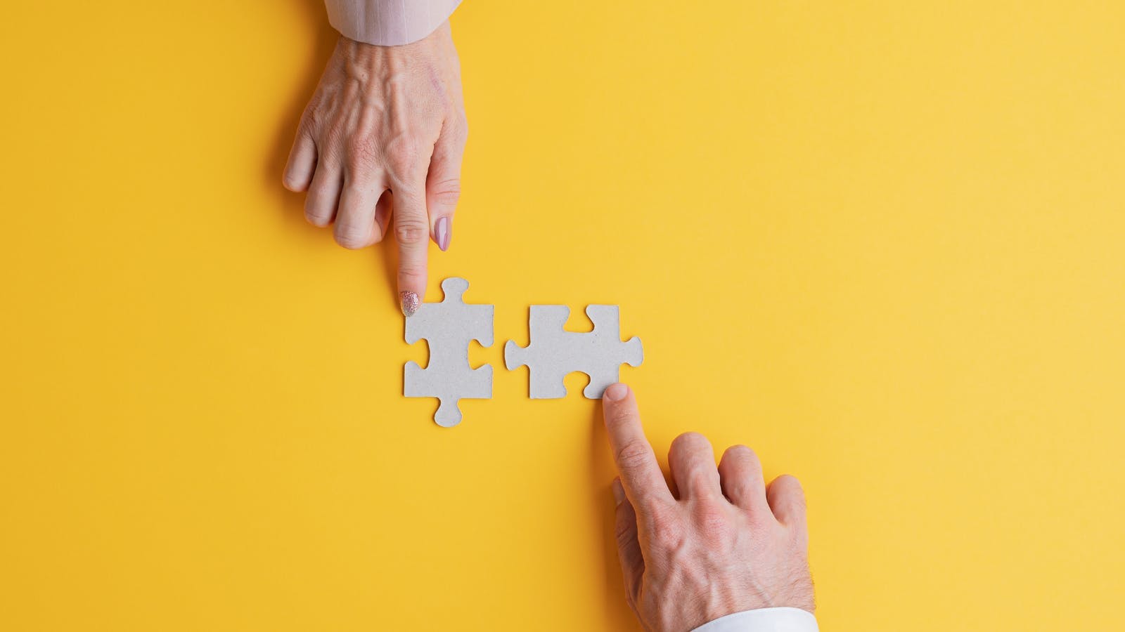 two hands pointing at two jigsaw puzzle pieces against yellow background