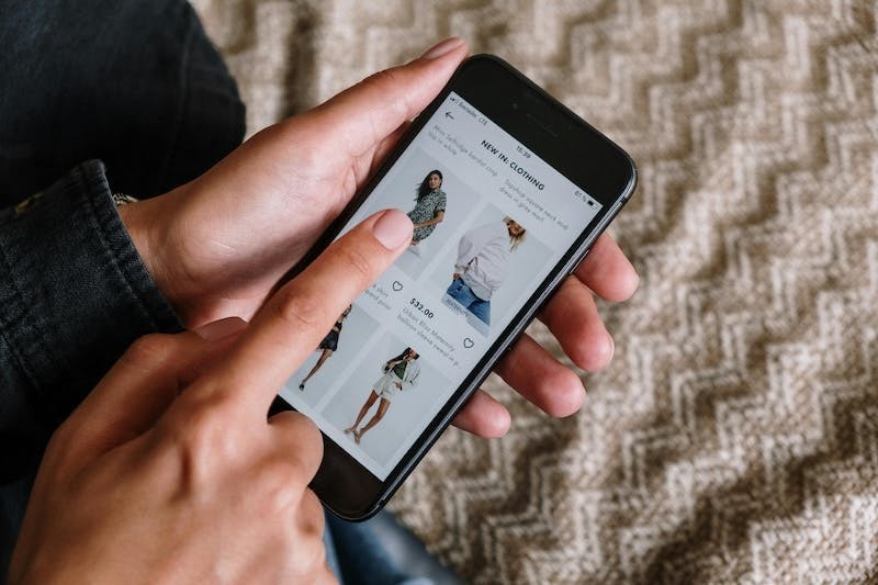 Eine Person hält ein Smartphone in der Hand und shoppt online nach Kleidung