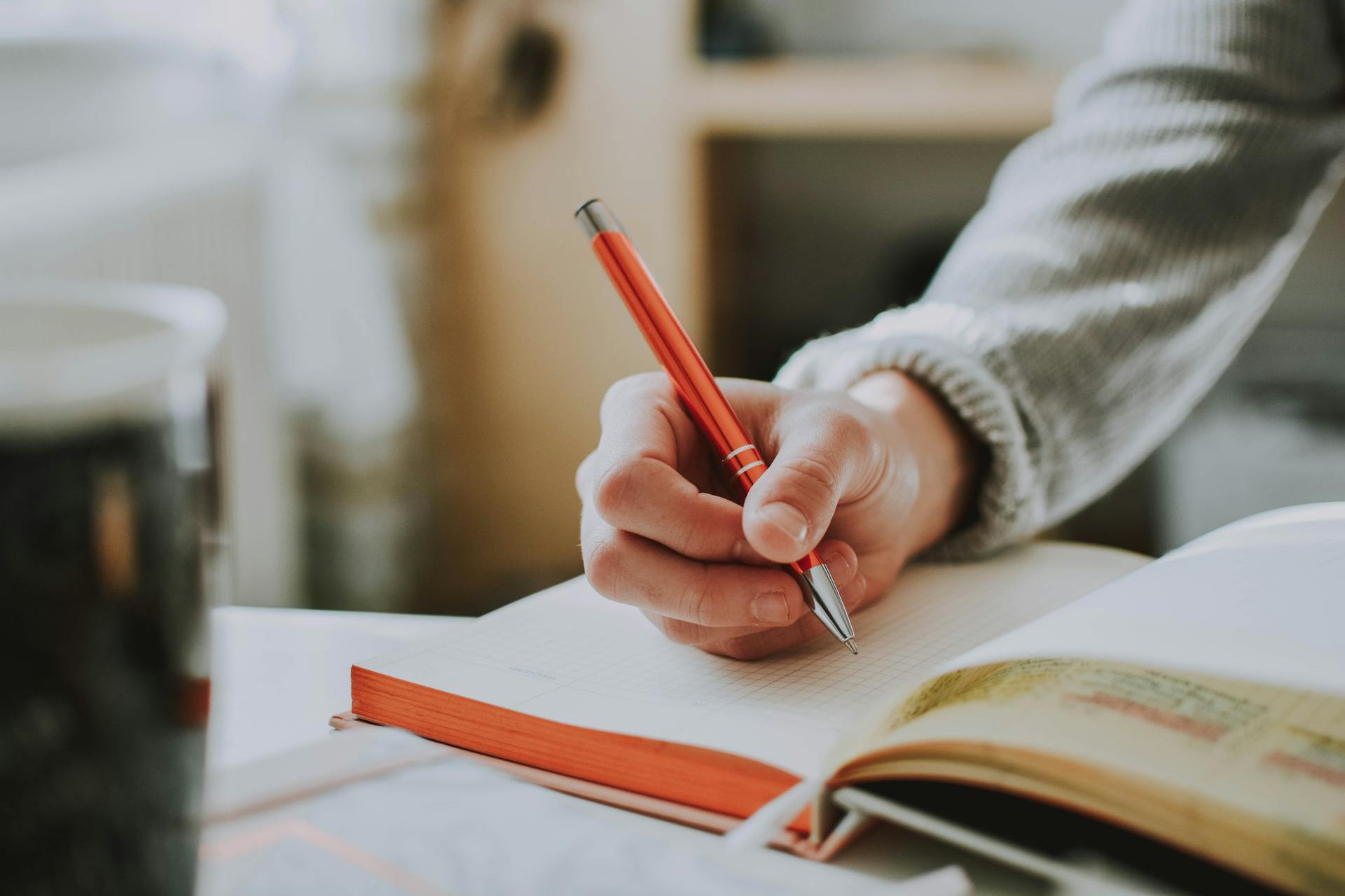 Person writing in a notebook with orange pen. Writing tips for content marketing success