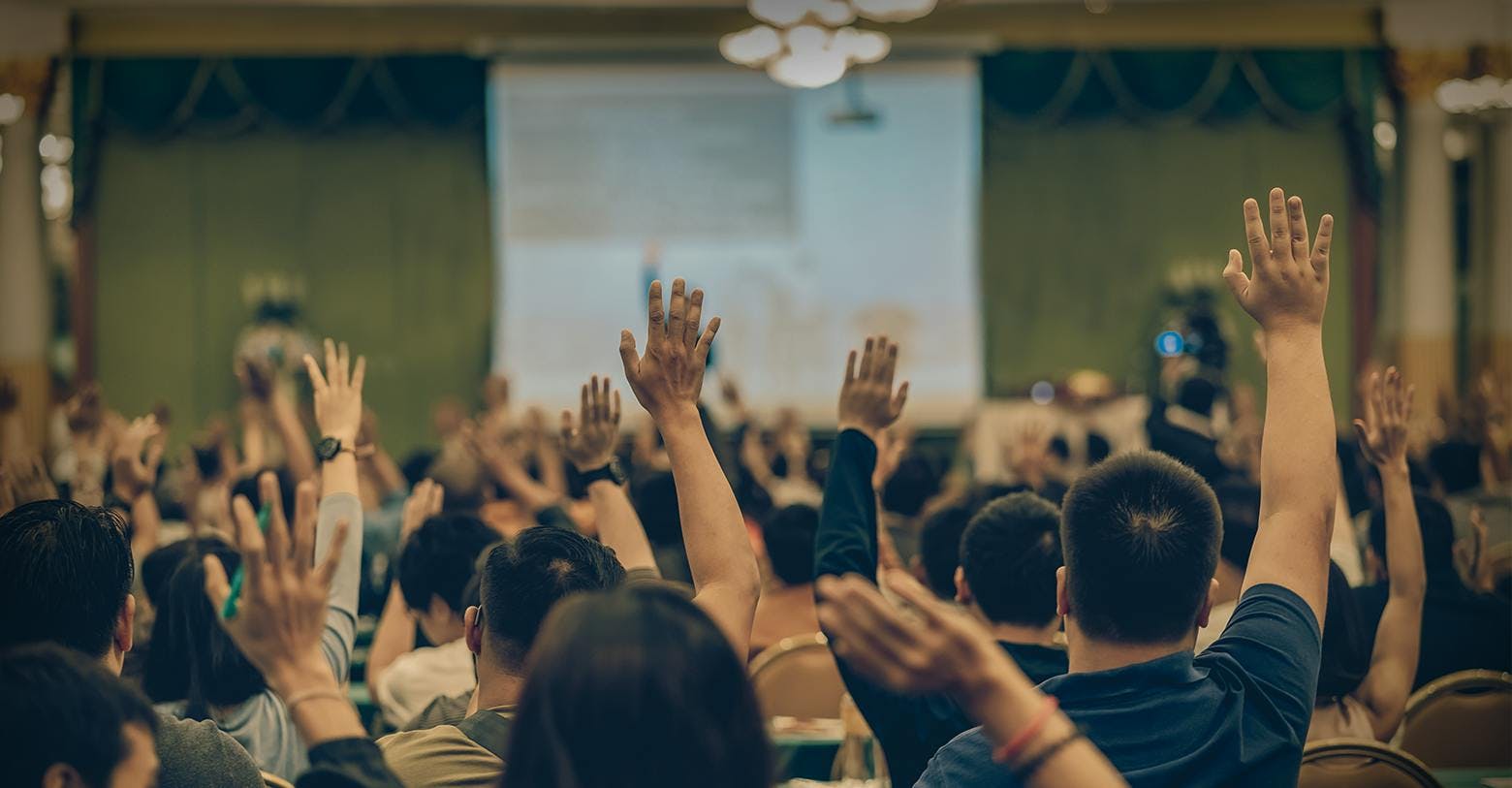 A room of people with hands in the air to ask questions